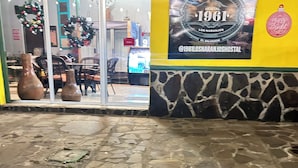 A storefront with a stone-tiled entrance, a large poster advertising 'Hostal 1961 Los Naranjos El Salvador', and two large vases outside.