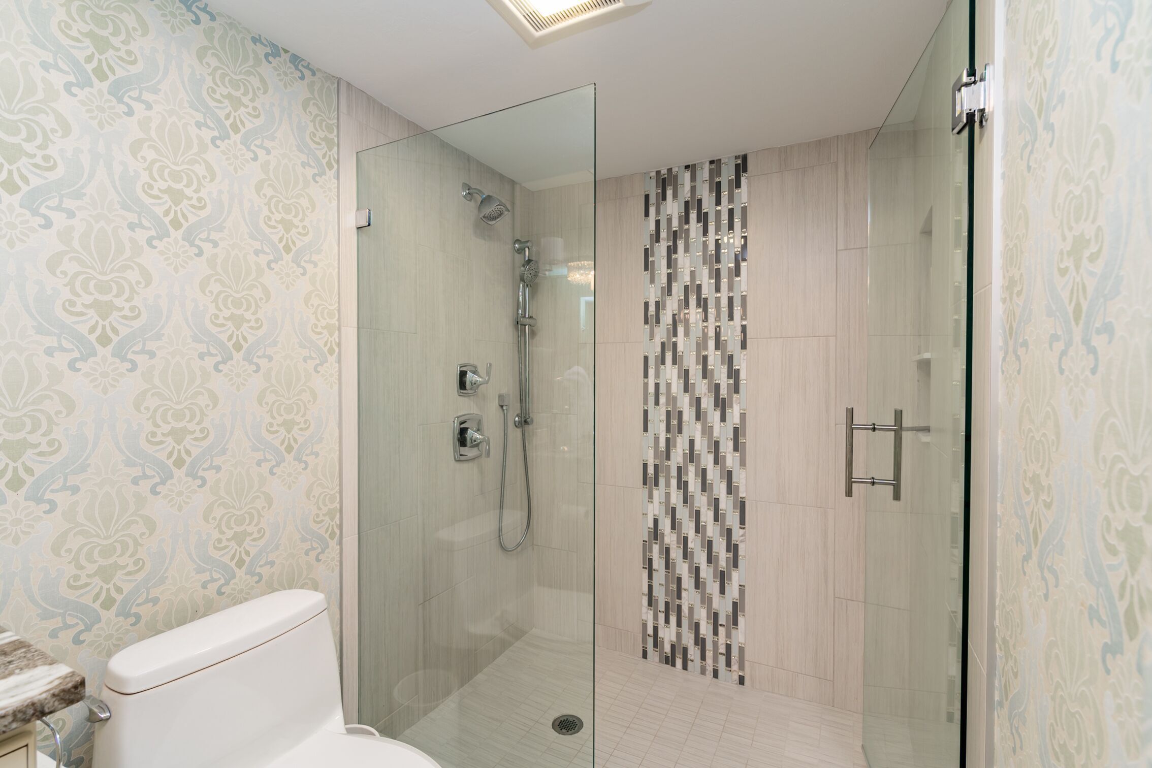 A modern bathroom with a glass-enclosed shower, patterned wallpaper, and a tiled floor.