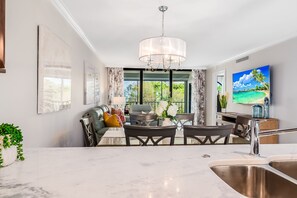 A modern kitchen with a marble countertop, stainless steel sink, and a dining area with a table and chairs. - Luxury Marco Island Condo/Walk to Beach/2BR/2BA/Pool +Parking (Marco Island)