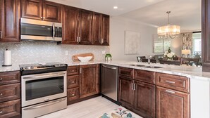 Una cocina moderna con armarios de madera oscura, electrodomésticos de acero inoxidable, salpicadero con motivo de espiga y encimera de mármol.