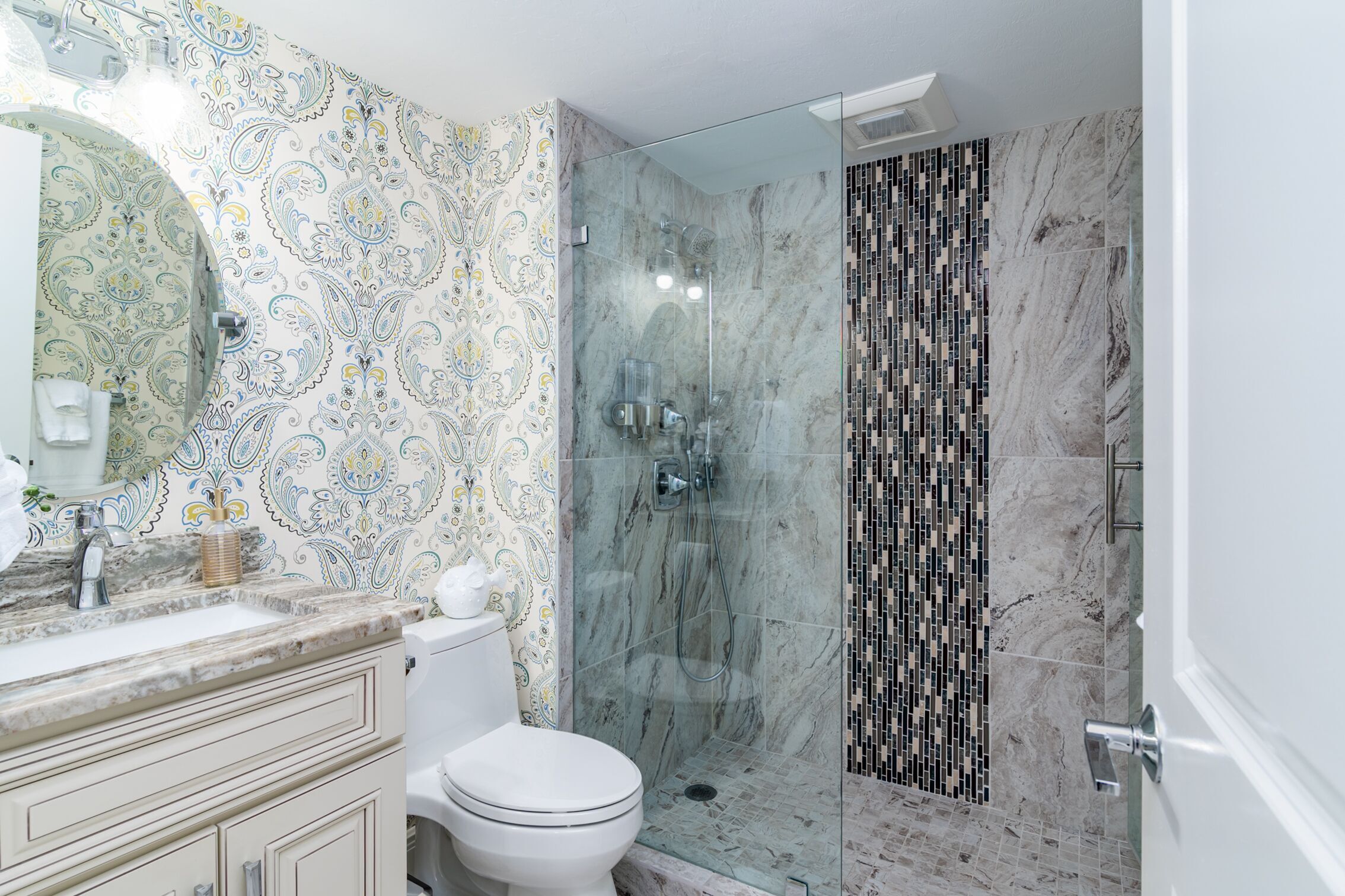 Une salle de bain avec un mur à motifs, une douche en verre et des toilettes blanches.