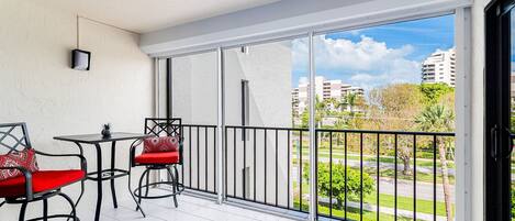 A balcony with two chairs and a table, a view of a cityscape, and a clear sky.
