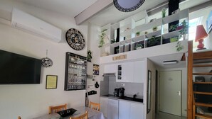 Eine kleine Küche mit weißen Schränken, einem Esstisch mit Stühlen, einem Fernseher und einer dekorativen Uhr.