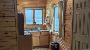 Una cucina compatta con pareti in legno, un lavandino, mobili, un cestino e una porta.