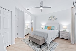 Een slaapkamer met een bed, nachtkastjes, een bankje, een plafondventilator en een wanddecoratie.