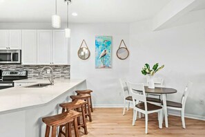 Een moderne keuken met witte kasten, een centraal eiland met krukken, en een eethoek met witte stoelen en een tafel.