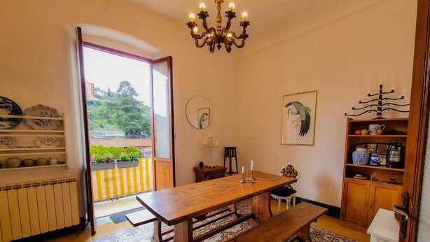 A dining area with a wooden table and benches, a chandelier, a view through an open door, and a patterned floor.