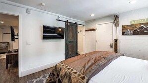 Un dormitorio con cama, televisor montado, puerta corredera tipo granero y un cuadro colgado.