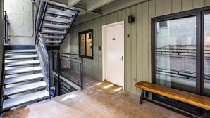 Una escalera con barandillas de metal, un banco, una puerta con un número y una ventana con vistas al exterior.