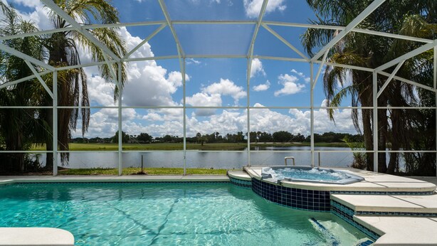 Una piscina con un jacuzzi, rodeada por una zona techada con palmeras y vistas a un lago.
