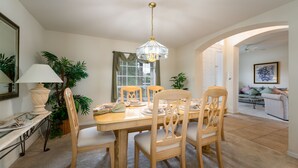 Un comedor con una mesa de madera, sillas, una lámpara de araña y una ventana con persianas.