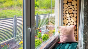 Une pièce avec une fenêtre donnant sur un jardin, un mur en bois brut et un banc rembourré avec un coussin.