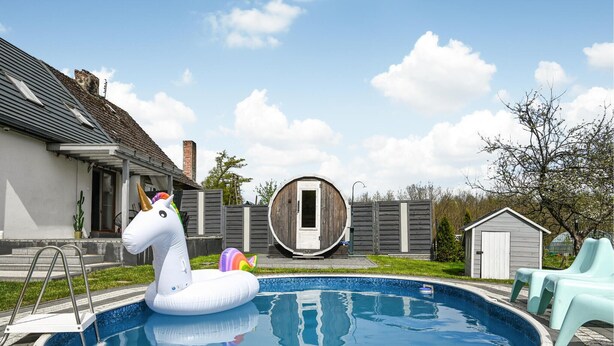 Un jardin avec une piscine, un flotteur en forme de licorne, un tonneau en bois et un petit abri de jardin.