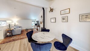 Un salon spacieux avec une table ronde en marbre et des fauteuils en velours bleu, un canapé gris et un tapis à motifs.