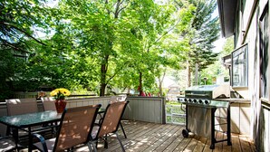 An outdoor patio with a table and chairs, a grill, and a wooden deck.