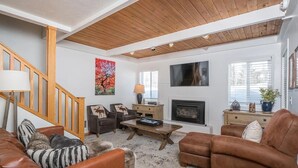 A living room with a fireplace, wooden ceiling, and a staircase.