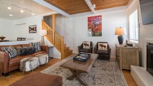 A living room with a wooden staircase, leather sofa, patterned rug, and a fireplace.