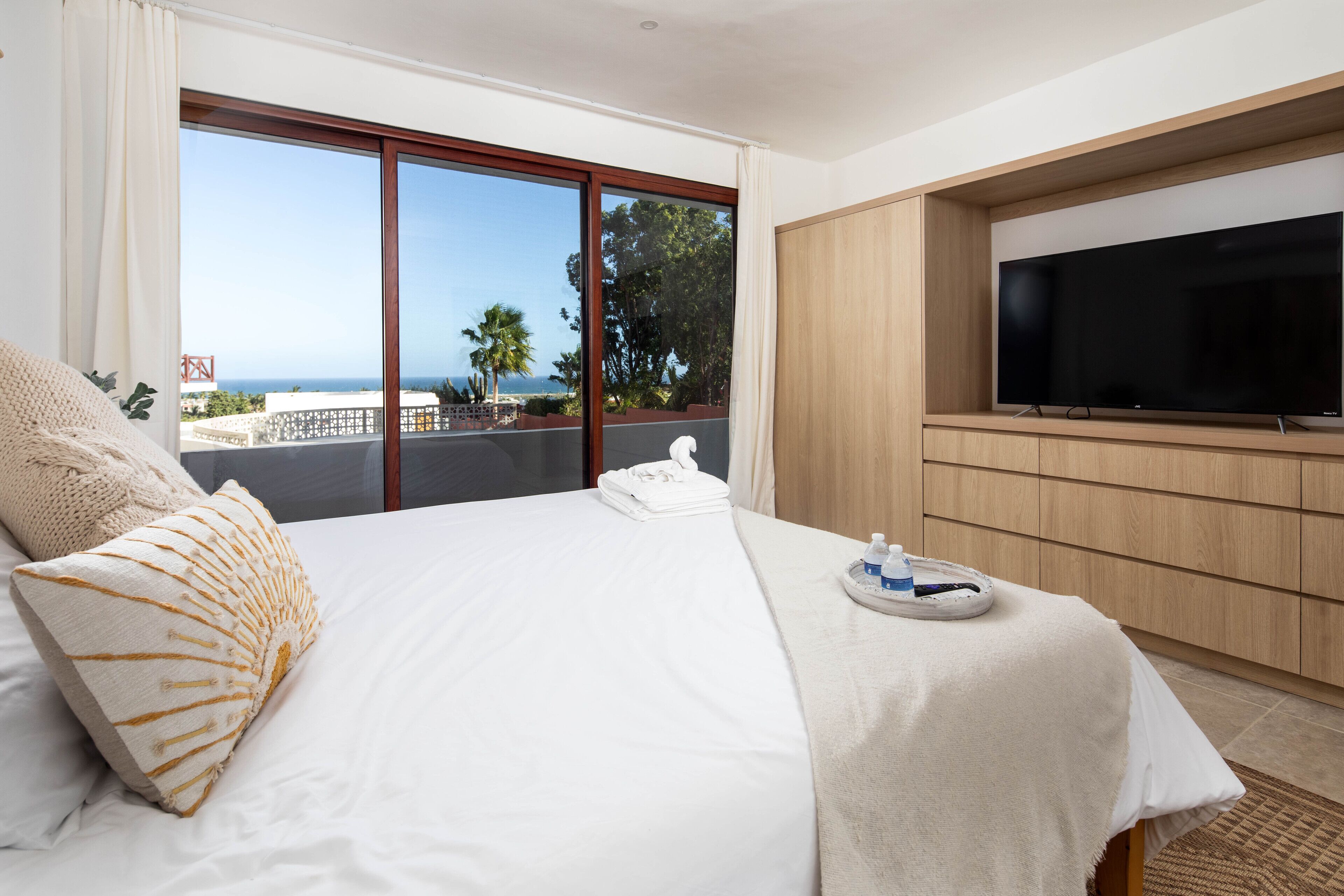 A hotel room with a large bed, a flat-screen TV, and a balcony with a view of the sea.