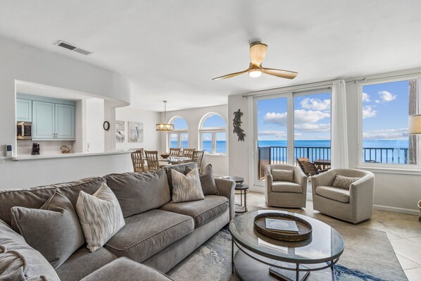 A spacious living room with a large gray sofa, two armchairs, a coffee table, and a ceiling fan.