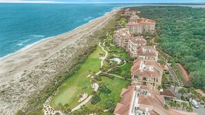 Vista aérea de un hotel costero con varias construcciones, un campo de golf y una playa.
