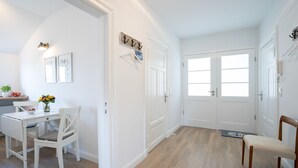 A bright, white interior with a dining area, a coat rack, and a door with a window.