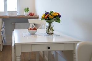 A white dining table with a bowl of fruit and a vase of flowers.