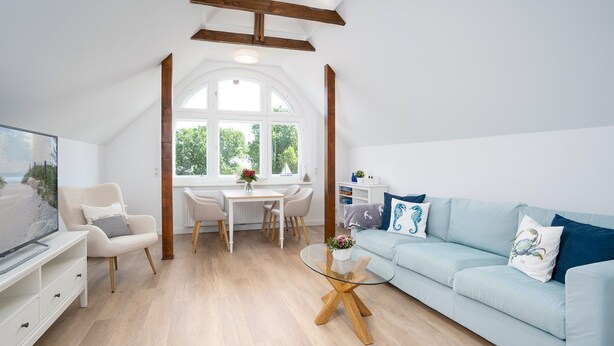 A modern living room with a high ceiling, a dining area with a table and chairs, a light blue sofa, and a TV on a white cabinet.