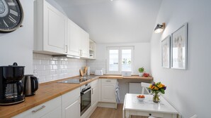 A compact kitchen with white cabinets, a wooden countertop, a coffee maker, and a dining area with a table and chairs.