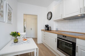 A modern kitchen with white cabinets, a wooden countertop, a built-in oven, and a coffee maker.