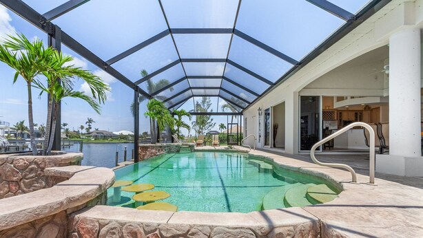 Una piscina cubierta con paredes de piedra y palmeras, conectada a un edificio con techo de cristal.