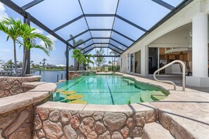 A covered swimming pool with stone walls and palm trees, connected to a building with a glass ceiling. - Dock with Tiki, Gulf Access, Heated Pool and Spa, -  Villa Baydream Believer - Roelens Vacations (Cape Coral)