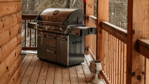 Una terraza de madera con una parrilla, un farol y una barandilla de madera.