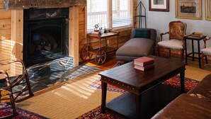 Una sala de estar acogedora con chimenea de piedra, paredes de madera y un ventilador de techo.
