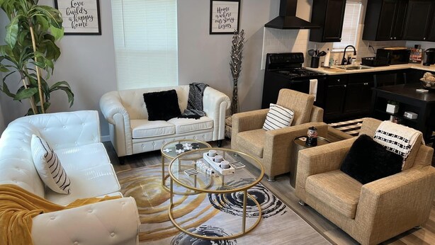 A living room with a white sofa, beige armchairs, a glass coffee table, and a large plant.