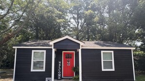 A small, two-story house with a red door and a 'Welcome' sign.