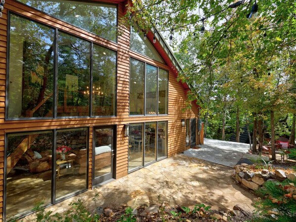 Una casa moderna con amplios ventanales, un patio de piedra y un jardín.