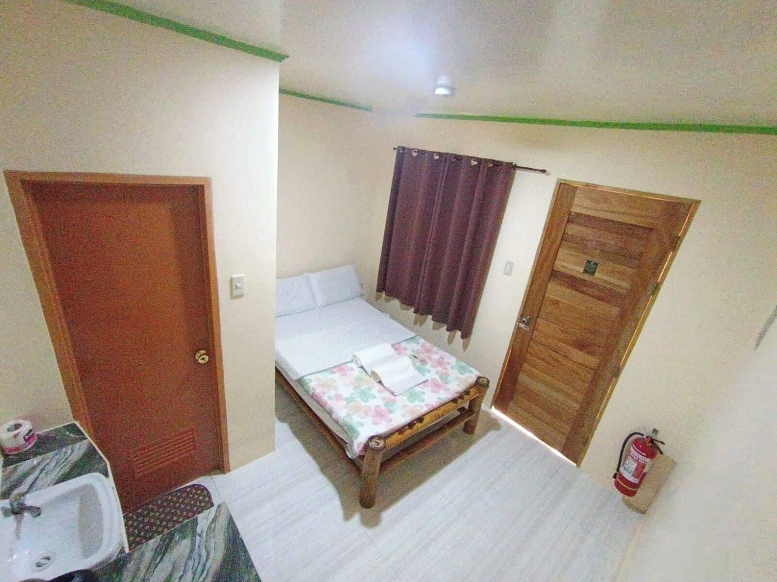 Una habitación de hotel pequeña y sencilla, con cama, armario de madera, baño con lavamanos y extintor.