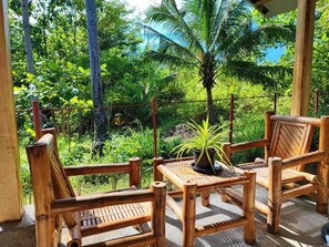A wooden deck with two chairs and a table, surrounded by a bamboo fence, overlooking a lush tropical garden. - Rose Apartments (Anda)