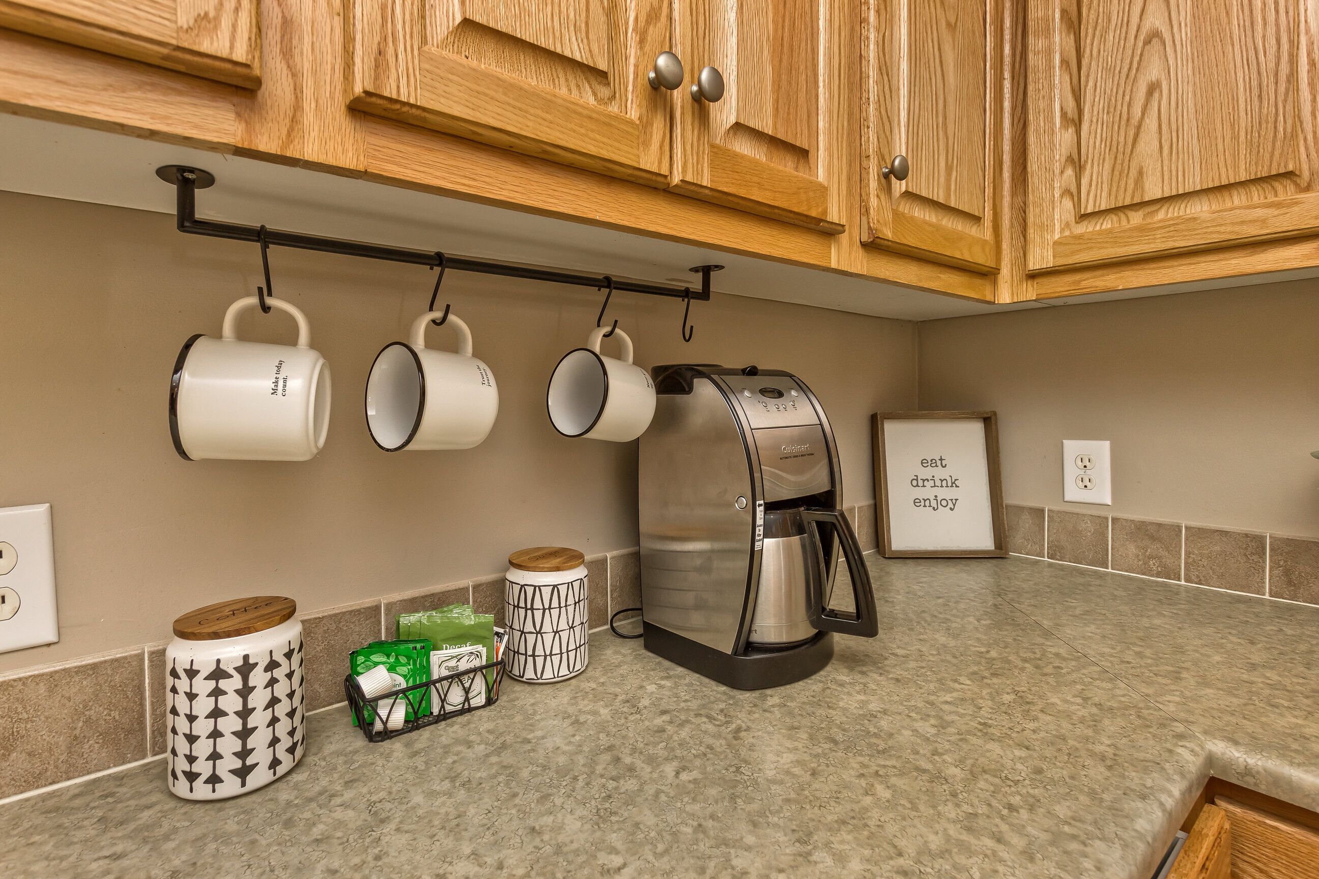 Una cocina con armarios de madera, una cafetera y tazas colgadas.