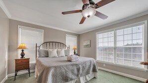Une chambre à coucher avec un lit, deux tables de chevet, un ventilateur de plafond et de grandes fenêtres.