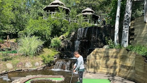 Een golf putting green met een kleine waterval en rieten gebouwen op de achtergrond.