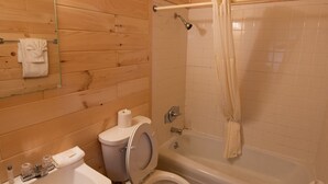 Un baño con paredes de madera, un lavabo, inodoro y una bañera con cortina de ducha.