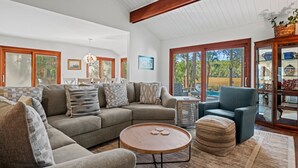 A spacious living room with a large sectional sofa, a round coffee table, and a blue armchair. There is a glass cabinet with decorative items and a view of the outdoors. - Pet Friendly ~ Marsh Views ~ Private Pool w/ Free Pool Heat ~ 25 Stoney Creek Rd (Hilton Head Island)