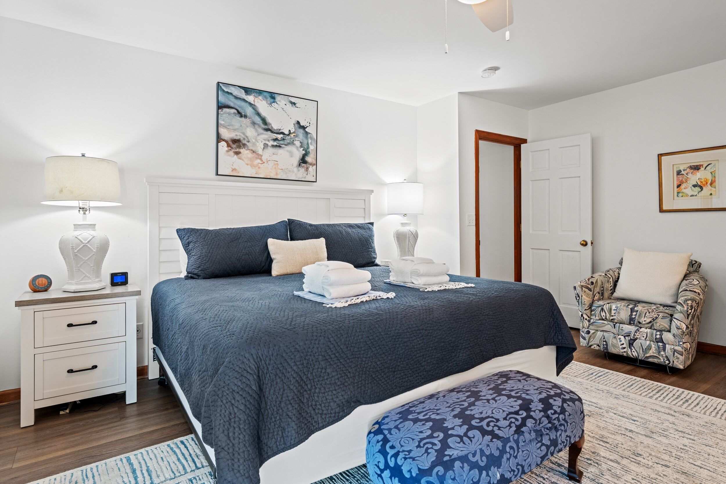 A bedroom with a large bed, two bedside tables, a chair, and a door.