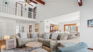 A spacious living room with a large sectional sofa, a round coffee table, and a blue armchair. A wooden ceiling fan is visible, and the room has a high ceiling with exposed beams. - Pet Friendly ~ Marsh Views ~ Private Pool w/ Free Pool Heat ~ 25 Stoney Creek Rd (Hilton Head Island)