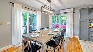 Un espace repas avec une longue table dressée pour six personnes, entourée de chaises, et un lustre moderne au-dessus.