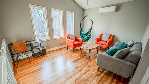 Un salon doté d’un parquet, de deux fenêtres, d’un fauteuil suspendu et d’un canapé.