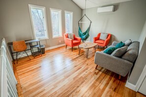 Un salon doté d’un parquet, de deux fenêtres, d’un fauteuil suspendu et d’un canapé.
