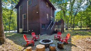 Une cabane rustique avec un foyer et des chaises rouges, située dans une zone boisée.