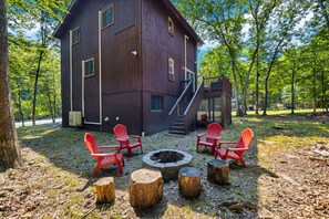 Eine rustikale Holzhütte mit Feuerstelle und roten Stühlen in einem bewaldeten Gebiet.